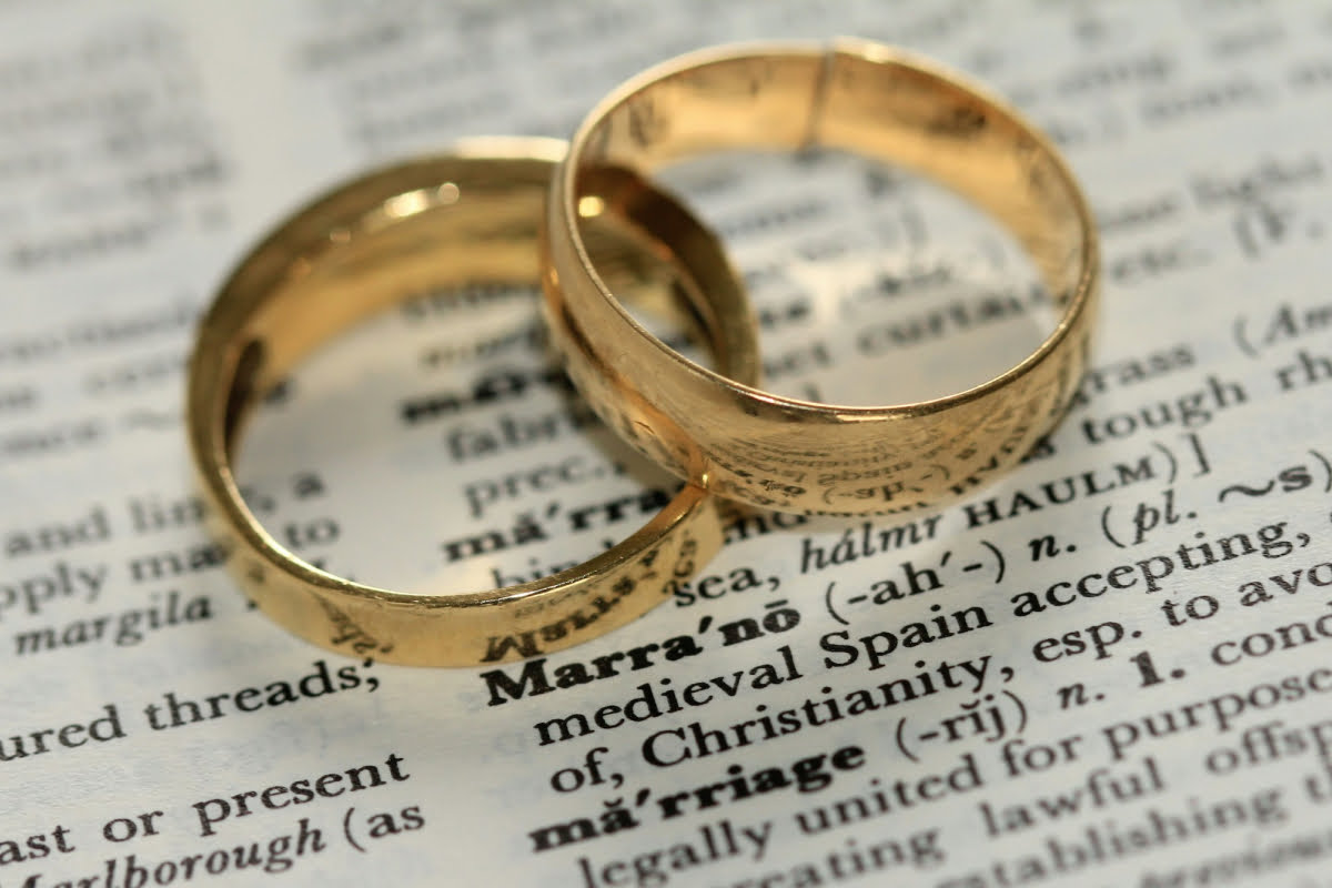 two gold wedding rings, sitting on a dictionary, page shows dictionary definition of marriage